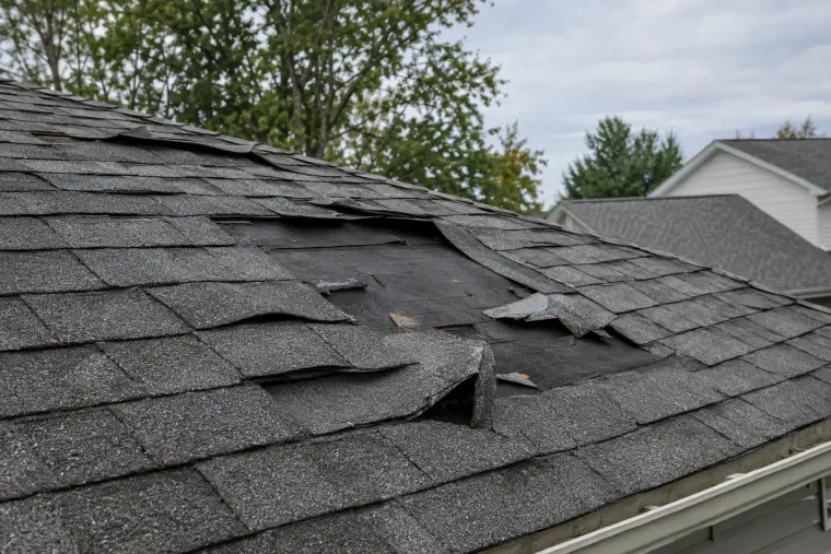 Roof after a wind storm with shingles bent back and two missing.