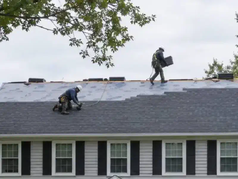 Roofers replacing shingles on a colonial house Two roofers replacing shingles on the roof of a white colonial house.