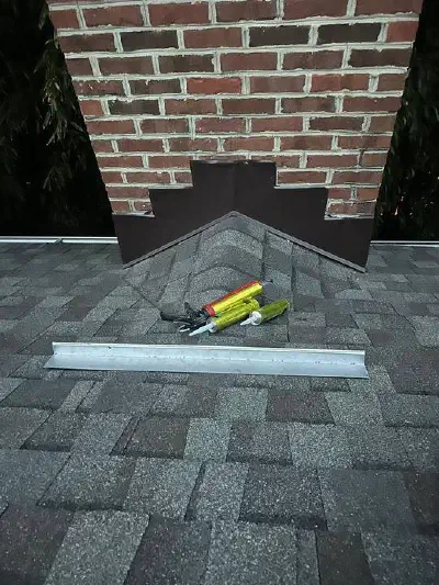 Brick chimney with new metal flashing where it meets the gray shingle roof.
