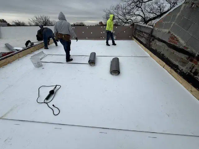 Roofing crew rolling out new white membrane across a flat roof.