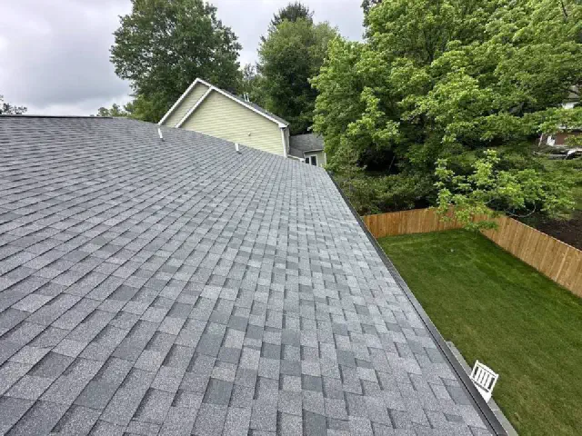 New gray shingle roof above a fenced backyard lawn and tall trees.