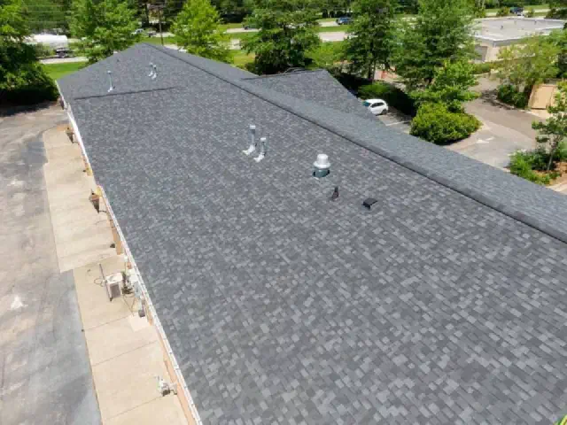 Long new gray shingle roof with roof vents on a low building.