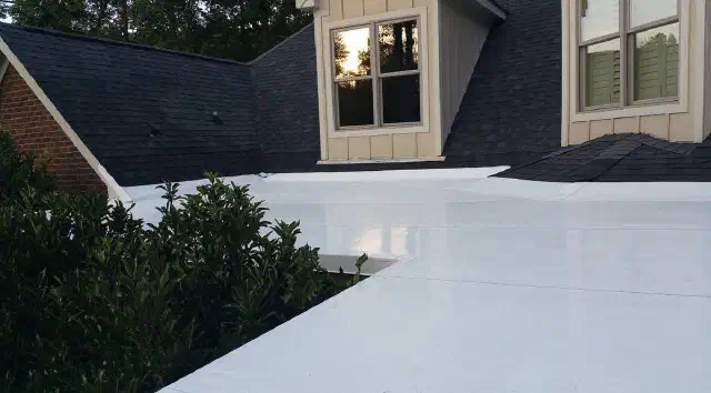 New white flat roof between a shingled dormer wall and a green shrub.