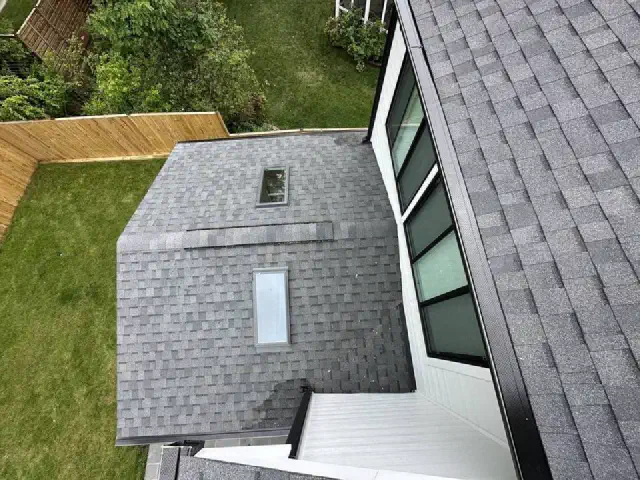 Gray shingle roof with two skylights beside a white house wall.