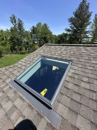Skylight with metal flashing around its frame set into a brown shingle roof.